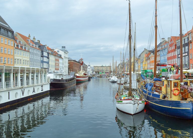 Barcos parados no canal no porto de Copenhague, com casas coloridas nas duas margens.