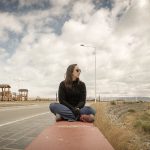 Rachel sentada em mureta em dia nublado.
