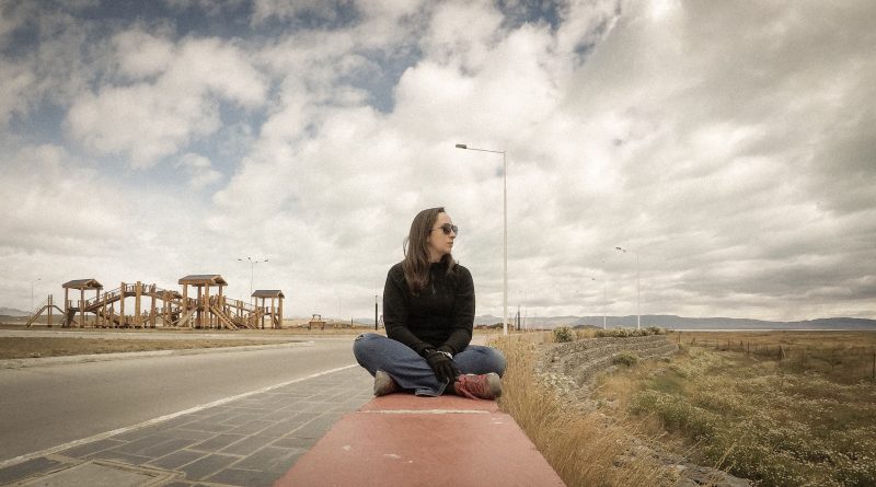 Rachel sentada em mureta em dia nublado.