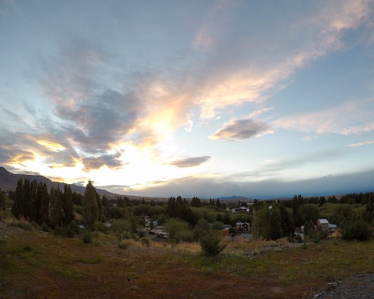 Paisagem de campo com árvores e casas, com claridade de fim de tarde.