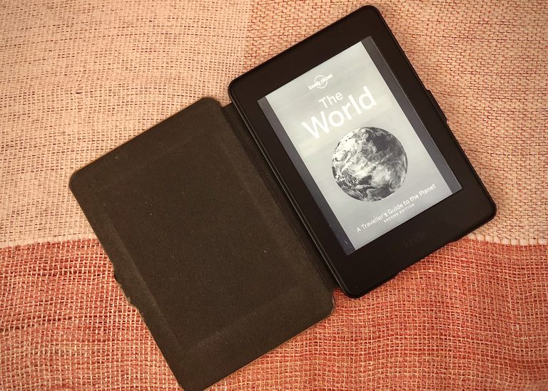 Kindle aberto com display que mostra capa de guia de viagem sobre o mundo.