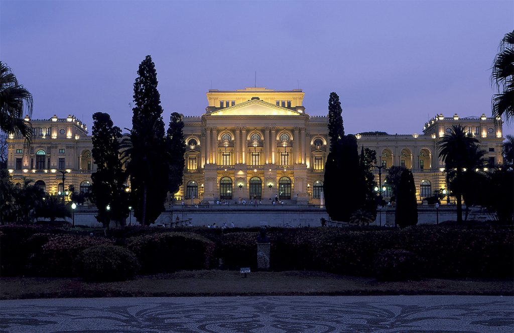 Fachada do Museu do Ipiranga à noite, iluminado com luzes no prédio.